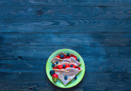 Fresh homemade crepes served on a plate with strawberries and blueberries, on a dark wooden background, free space for text.の写真素材