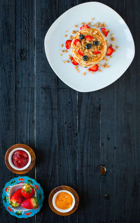 Homemade pancakes with fresh berries, strawberries, blueberries and maple syrup on a dark wooden background. Free space for textの写真素材
