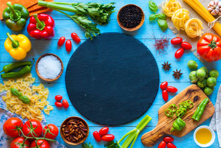 Top view of a wooden table full of italian pasta ingradients like peppers, tomatoes, olive oil, basil,  garlic and several spices.の写真素材