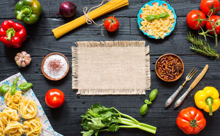 Top view of a wooden table full of italian pasta ingradients like peppers, tomatoes, olive oil, basil,  garlic and several spices.の写真素材