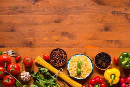 Top view of a wooden table full of italian pasta ingradients like peppers, tomatoes, olive oil, basil,  garlic and several spices.の写真素材