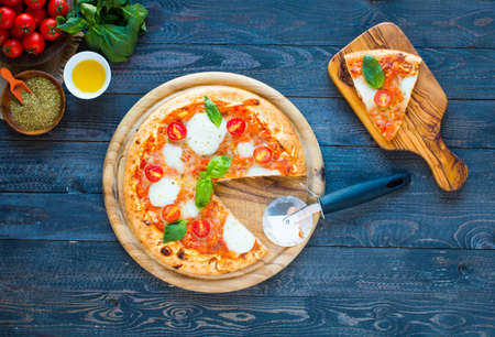 Top view of italian classic pizza margherita over a wooden table with toppings like tomatoes, basil, oregano.の写真素材