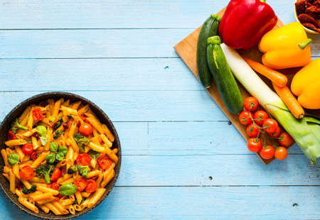 Italian penne pasta in tomato sauce and different type of vegetables, on a wooden background, free space for textの写真素材