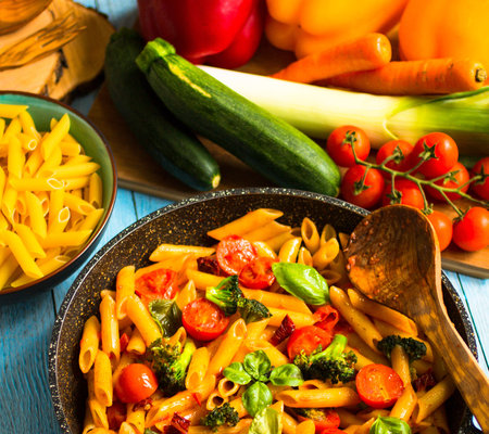 Italian penne pasta in tomato sauce and different type of vegetables, on a wooden background, free space for textの写真素材