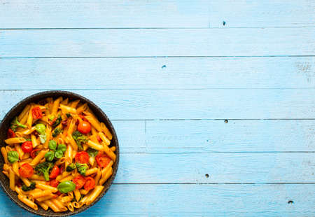 Italian penne pasta in tomato sauce and different type of vegetables, on a wooden background, free space for textの写真素材