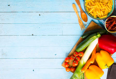 Italian penne pasta in tomato sauce and different type of vegetables, on a wooden background, free space for textの写真素材