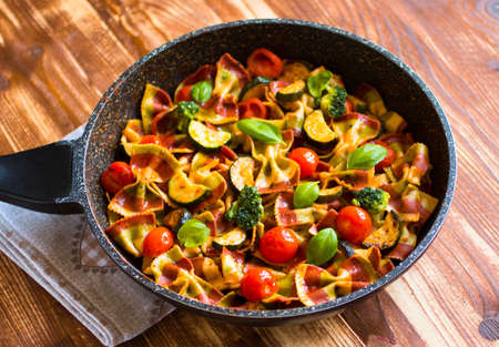 Italian pasta farfalle in tomato sauce and various type of vegetables on a wooden background, free space for text. Top viewの写真素材