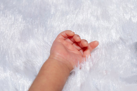 Newborn baby hand on a white fur background. Close-up.