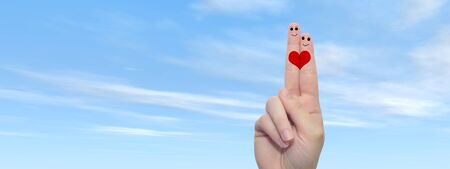 Conceptual fingers in love over blue sky with a heart painted bannerの写真素材