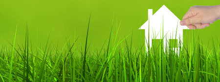 Concept or conceptual white paper house symbol held in hand by a woman in green summer grass background bannerの写真素材