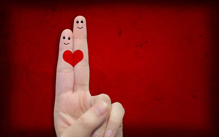 Conceptual fingers in love, with a painted heart shape over red old paper backgroundの写真素材