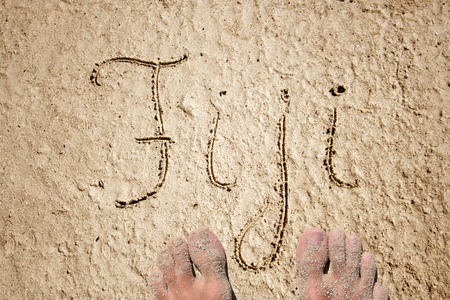 Concept or conceptual Fiji handwritten in sand on a beach background with feet in an exotic islandの写真素材