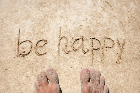 Concept or conceptual Be happy text handwritten in sand on a beach with feet in an exotic islandの写真素材