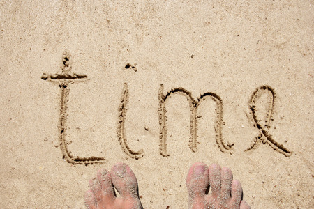 Concept or conceptual hand drawn time text carved in a golden sandy beachの写真素材