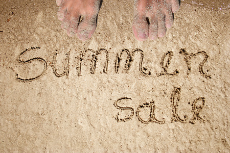 Concept or conceptual summer sale text handwritten in sand on a beach with feet in an exotic islandの写真素材