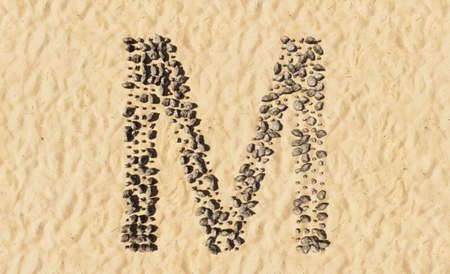 Concept or conceptual stones on beach sand handmade symbol shape, golden sandy background, sign of M. 3d illustration metaphor for education, nature, summer, sunny, seaside and tropicalの写真素材