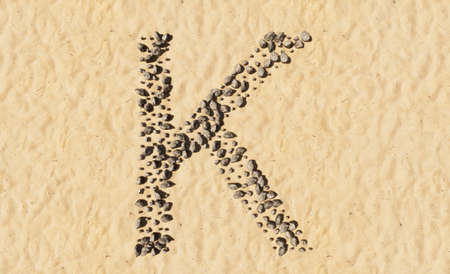 Concept or conceptual stones on beach sand handmade symbol shape, golden sandy background, sign of K. 3d illustration metaphor for education, nature, summer, sunny, seaside and tropicalの写真素材