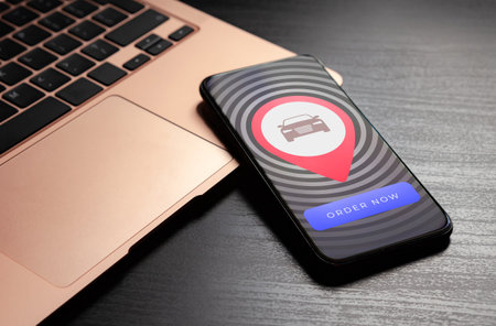 Order the taxi or carsharing service application concept. Rent a car online using a mobile app. On the smartphone screen, a geo-tag with a car icon and a Order Now buttonの写真素材