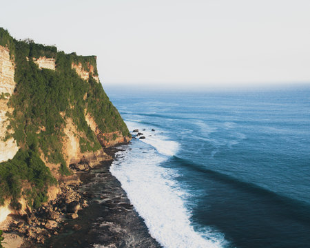 Aerial view Bali cliffs meet crashing ocean waves along Uluwatu coastline, turquoise Bali sea under misty horizon, natural beauty and serene tropical paradise in Indonesia scenic island landscapesの写真素材