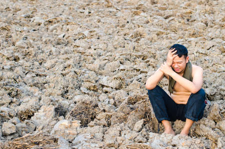 Frustrated and sad young man without a shirt sitting in barren groundの写真素材