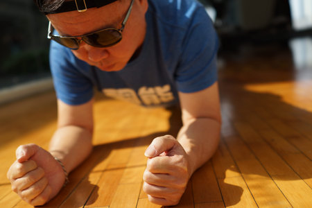 Overweight man doing plank exercise in a gym with wooden floor by a pool - Horizontal