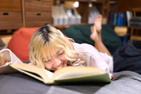 Cheerful Long-haired Asian girl was reading a book while relaxing on soft bean bag at home. Horizontalの写真素材