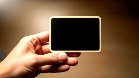 A close-up of a hand presenting an empty dark rectangular card with a light wooden frame, ideal for custom text, branding, or promotional messages.の素材