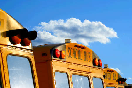 back of parked school busses in the parking lot against a beautiful sky with cloudsの写真素材