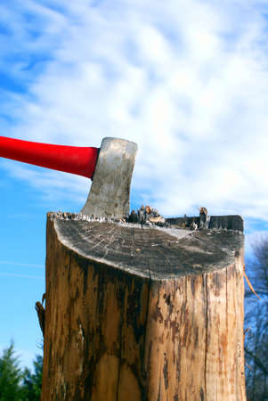 Axe in a splitting log against beautiful blue sky with fluffy cloudsの写真素材
