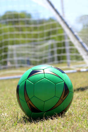 Green soccer ball with net in the background on dried out soccer field            の写真素材