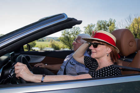 Happy older woman with a sun has a partner in a luxury convertible carの写真素材