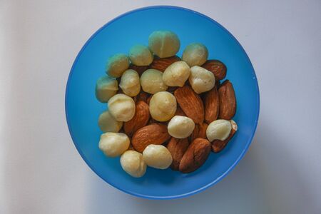 Macadamia and almonds mixed roasted nuts top closeup view. Collection of healthy nuts served on a blue plastic bowl.の写真素材