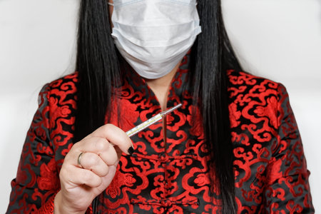 Coronavirus COVID-19 concept with female wearing mask holding thermometer. Woman in Asian clothes,...