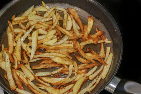 Frying French fries in hot olive oil at home kitchen close up. Top view of preparing fresh cut house...