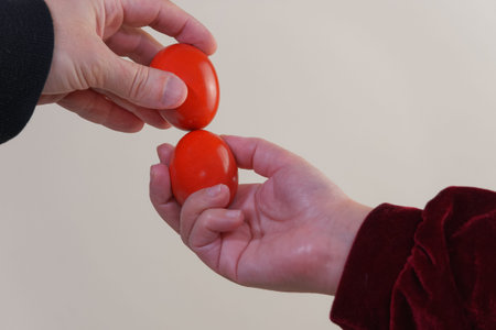 Red hard-boiled eggs tapping Happy Easter game closeup. Two unidentified people hold painted eggs...