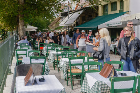 Athens, Greece Crowd around half empty restaurant tables. Monastiraki area with tourists along tavern outdoors seating area with wooden green chairs.のeditorial素材