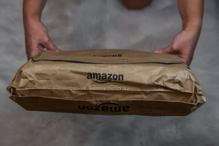 Thessaloniki, Greece - November 23 2020: Amazon brand online delivery box concept. Hand holds delivered order package with company logo of multinational technology e-commerce company.のeditorial素材
