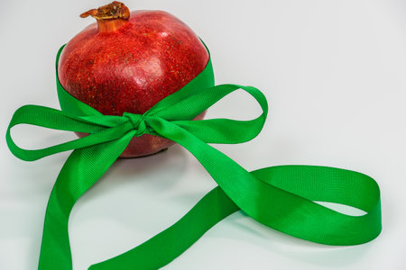 A pomegranate with a green ribbon as a new year gift against white background. Red fresh fruit with green ornamental decoration and copy space.の写真素材