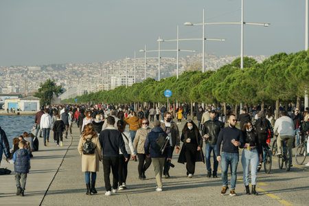 Thessaloniki, Greece - February 6 2021: Very Large number of people with covid-19 masks outdoors. Unidentified persons with face protection walk at close distance on pedestrian area of city waterfrontのeditorial素材