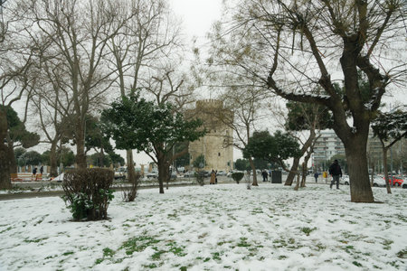 Thessaloniki, Greece - February 14 2021: Medea front hits with heavy snowfall city center, with crowd moving. People in warm clothes and covid-19 masks around White Tower landmark with snow falling.のeditorial素材