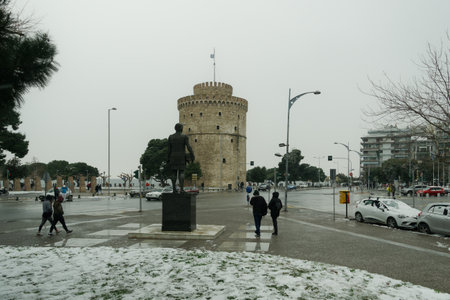 Thessaloniki, Greece - February 14 2021: Medea front hits with heavy snowfall city center, with crowd moving. People in warm clothes and covid-19 masks around White Tower landmark with snow falling.のeditorial素材