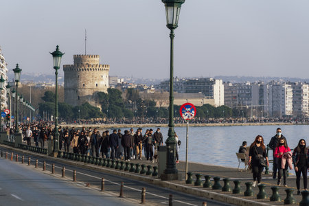 Thessaloniki, Greece - February 27 2021: People with covid-19 masks before the city landmark. Large crowd with face protection walks at the waterfront area of the White Tower.のeditorial素材