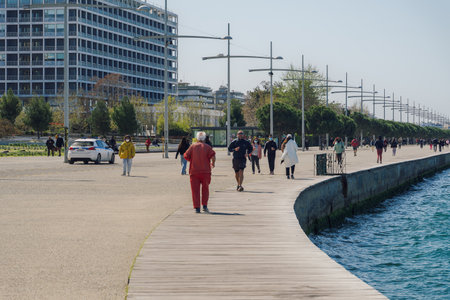 Thessaloniki, Greece - April 09 2021: Greek police car patrolling if people wear covid-19 masks outdoors. Unidentified persons with face protection walk on the pedestrian area of the city waterfront.のeditorial素材