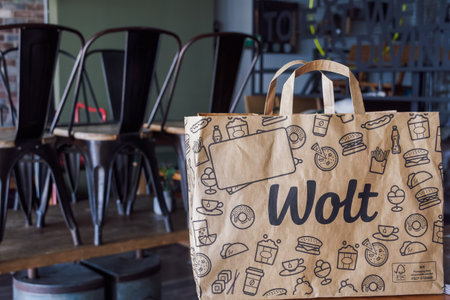 Thessaloniki, Greece - April 02 2021: Wolt food delivery bag with company logo, on restaurant. Finish company paper bag with handle, used by platform courier partners.のeditorial素材