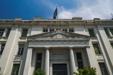 Thessaloniki, Greece - April 26 2021: Hellenic bank building facade against blue sky. Day view of neoclassical monument of branch of Alpha Bank Greece with sign at Mitropoleos street.のeditorial素材