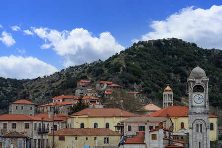 Greek village with traditional low-rise houses against blue sky with clouds. Day view of historic settlement with red roof tiles residences and church bell tower in Dimitsana, Arcadia Peloponnese.の写真素材