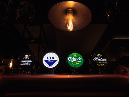 Thessaloniki, Greece - May 5 2022: Bar beer taps with various names and illuminated logos of brands including Fix Hellas, Carlsberg and Kaiser pilsner.のeditorial素材