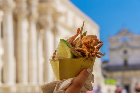 Holding Italian street fish food on a cone. Day view of a female hand that holds a greasy paper cone...