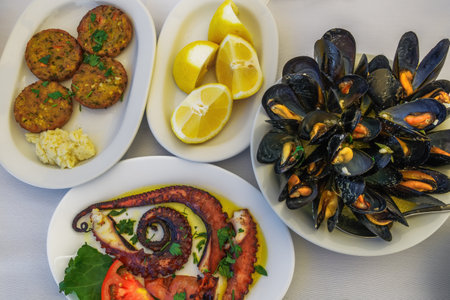 Greek tavern food closeup top view with mussels with clams, fried octopus seafood, lemon slices and zucchini fritters with garlic sauce.の写真素材