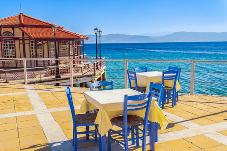 Empty tavern restaurant by the seafront with wooden chairs and tables under a bright sun in summer.の写真素材